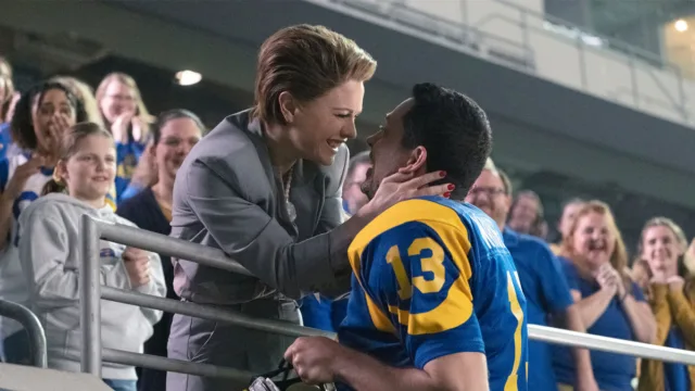 promotional still from American Underdog featuring zachary levi and anna paquin as their characters kissing in a football stadium