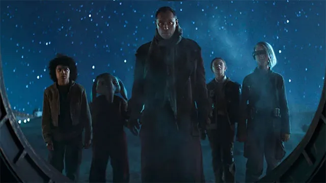the main cast of star wars skeleton crew featuring jude law in the center. all are in costume and standing in front of a starry night sky