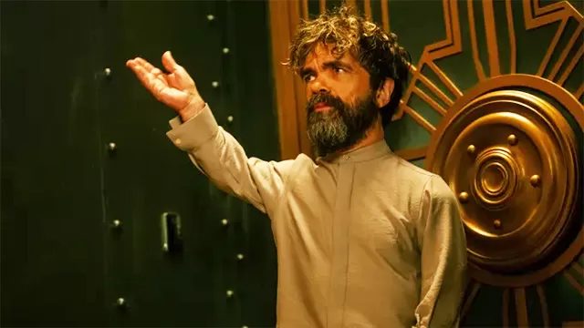 Peter Dinklage as Perry in Dexter: Resurrection, dramatic close-up portrait with raised hand gesture, curly beard, tan tunic, green door and ornate gold wheel backdrop, HBO crime thriller series 2025 revival