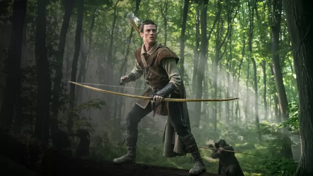 Robin Hood in misty Sherwood Forest from MGM+ 2025 series, bow drawn against Norman oppressors – exposing radical progressive anti-Christianity and anti-colonization metaphors in Hollywood's twisted medieval retelling.